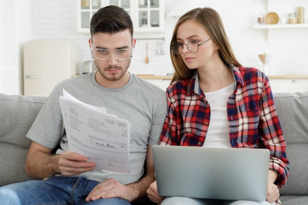 A young couple sitting on a sofa reviewing mortgage documents together, representing Ontario homeowners evaluating renewal options in 2025.