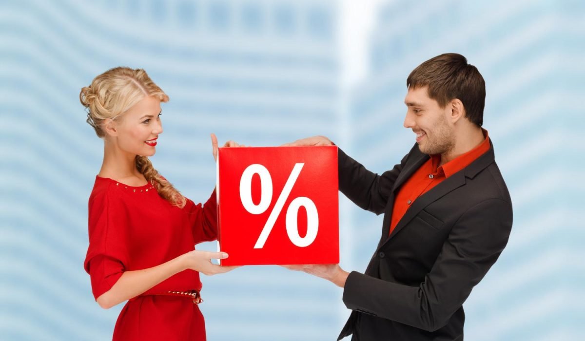 A man and woman smiling while holding a red cube with a white percent sign, symbolizing mortgage interest rates and loan offers.